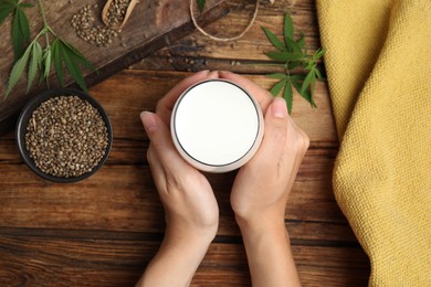 Woman with glass of hemp milk at wooden table, top view