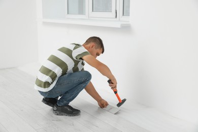 Photo of Professional worker using hammer during installation of new laminate flooring indoors