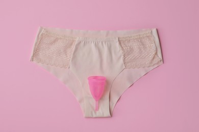 Panties and menstrual cup on pink background, top view