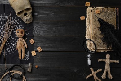 Voodoo doll with pins surrounded by ceremonial items on black wooden table, flat lay. Space for text