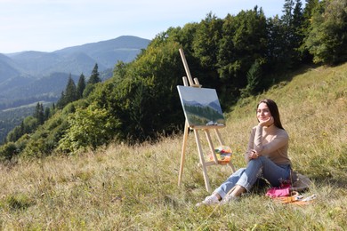 Young woman near easel with drawing in mountains, space for text