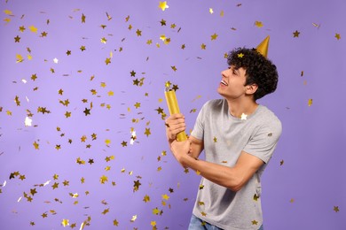 Photo of Handsome young man blowing up party popper on violet background