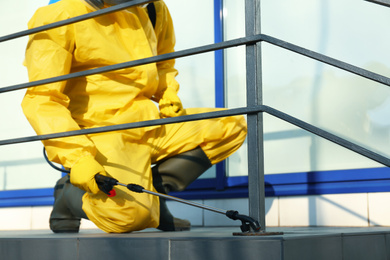 Male worker in protective suit spraying insecticide on stairs outdoors, closeup. Pest control