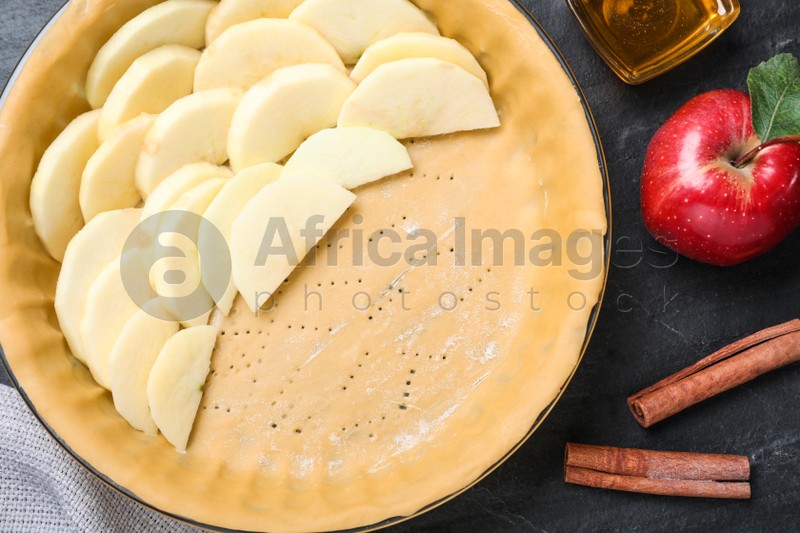 Dish with fresh apple slices and raw dough on black table, flat lay. Baking pie