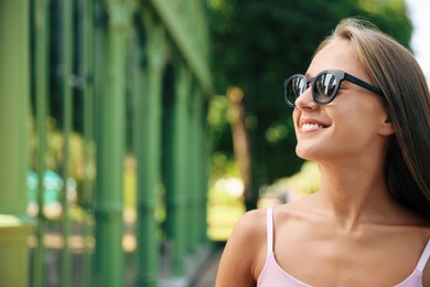 Photo of Beautiful young woman in stylish sunglasses on city street, space for text