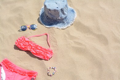 Jeans hat, sunglasses and bikini on sand, space for text. Beach accessories