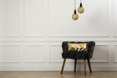 Stylish armchair with cushion near white wall indoors, space for text. Interior design