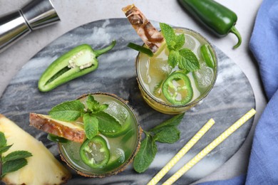 Photo of Glasses of spicy pineapple cocktail with jalapeno and mint on grey table, flat lay