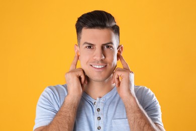 Man inserting foam ear plugs on yellow background