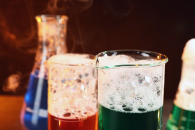 Photo of Laboratory glassware with colorful liquids and steam on black background, closeup. Chemical reaction