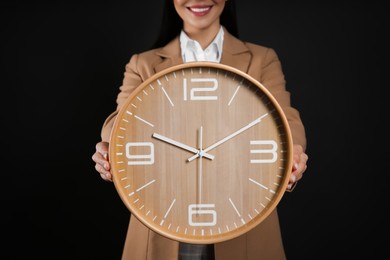Businesswoman holding clock on black background, closeup. Time management
