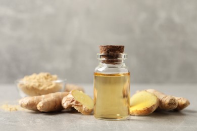 Photo of Glass bottle of essential oil and ginger root on grey table