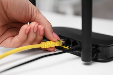 Woman connecting cable to router at white table, closeup. Wireless internet communication