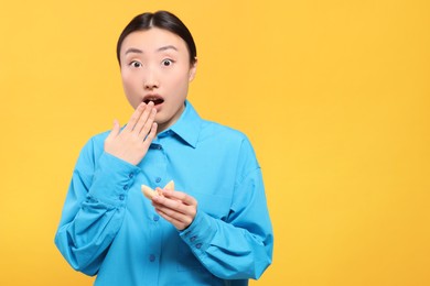Photo of Surprised asian woman holding tasty fortune cookie with prediction on yellow background, space for text