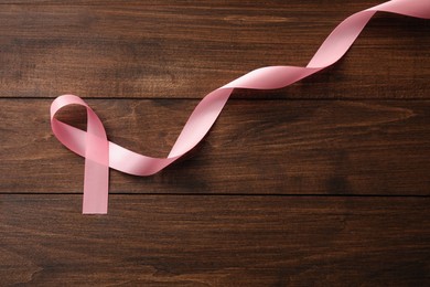 Pink ribbon on wooden table, top view with space for text. Breast cancer awareness concept