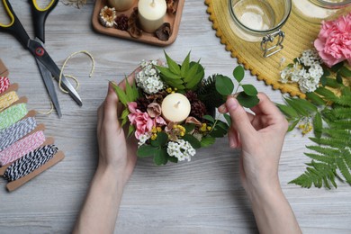 Photo of Woman making floral composition with candle at wooden table, top view. Master class