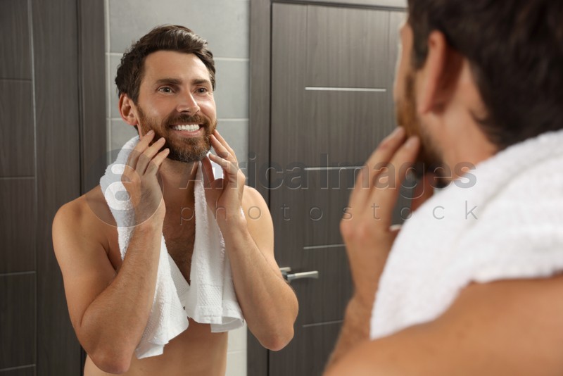 Handsome bearded man looking at mirror in bathroom near wooden doors