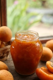 Photo of Jar of delicious jam and fresh ripe apricots on wooden table indoors. Fruit preserve