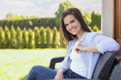 Portrait of beautiful young woman sitting on chair at backyard, space for text