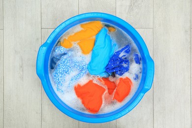 Basin with colorful clothes on floor, top view. Hand washing laundry