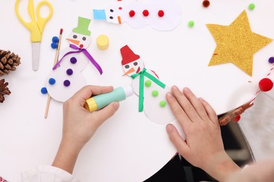 Little child making Christmas craft at white table, top view