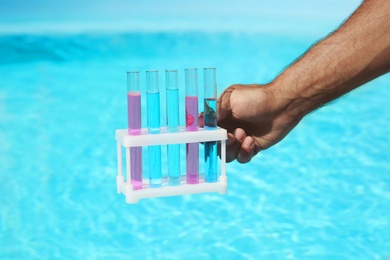Man holding test tubes with reagents near swimming pool, closeup