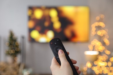 Woman with remote control in room decorated for Christmas, closeup