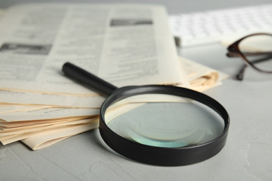 Magnifying glass and stack of newspapers on grey table, closeup. Job search concept