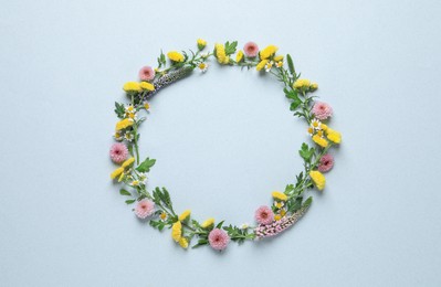 Wreath made of beautiful flowers and green leaves on light blue background, flat lay. Space for text