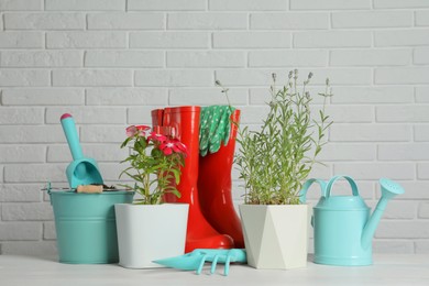 Photo of Beautiful flowers and gardening tools on wooden table near white brick wall