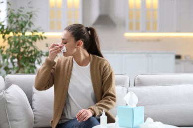 Photo of Ill woman with paper tissue sneezing at home
