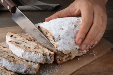 Woman cutting traditional Christmas Stollen at wooden board, closeup