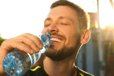 Photo of Happy man drinking water outdoors on hot summer day, closeup. Refreshing drink
