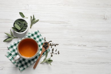 Cup of sage tea, green leaves and spoon on white wooden table, flat lay. Space for text