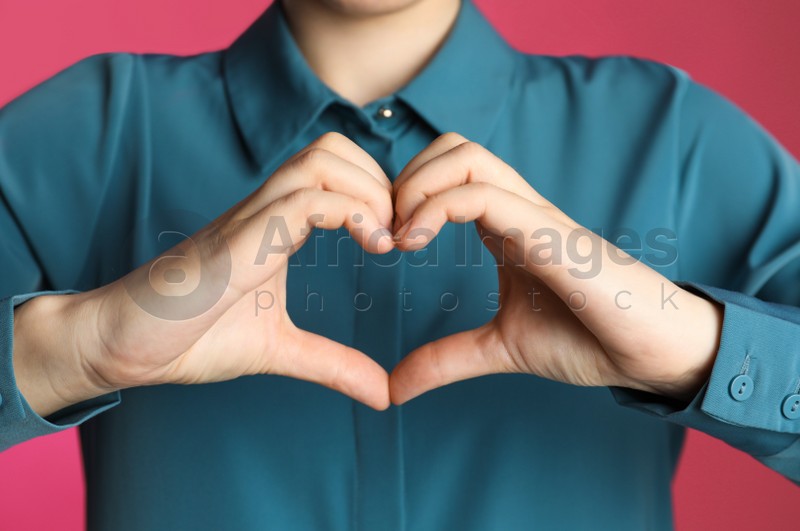 Woman making heart with her hands on pink background, closeup