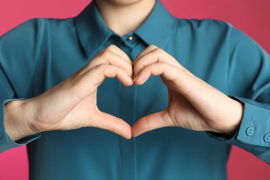 Photo of Woman making heart with her hands on pink background, closeup