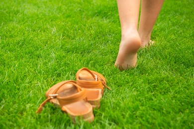 Woman leaving her shoes and walking away barefoot on green grass, closeup