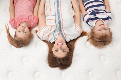 Mother and her children lying on new orthopedic mattress, top view