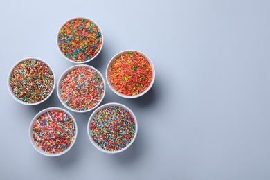 Colorful sprinkles in bowls on light grey background, flat lay with space for text. Confectionery decor