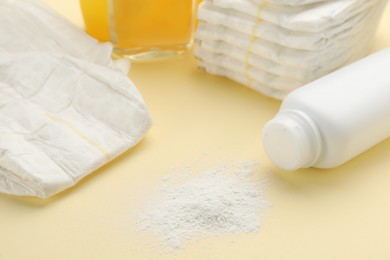 Photo of Bottle, scattered dusting powder and diapers on beige background. Baby care products