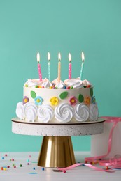 Delicious birthday cake and party decor on white wooden table against turquoise background