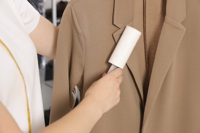 Woman using adhesive lint roller indoors, closeup. Dry-cleaning service