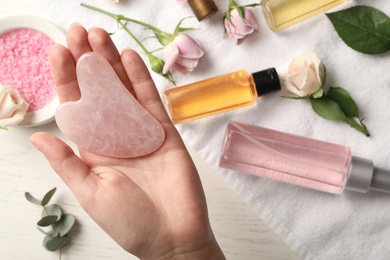 Photo of Woman with rose quartz gua sha tool at white wooden table, top view