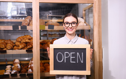 Photo of Female business owner holding OPEN sign in bakery