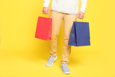 Young man with paper bags on yellow background, closeup