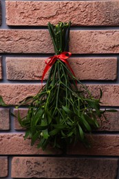 Mistletoe bunch with red bow hanging on brick wall. Traditional Christmas decor