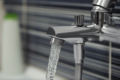 Water flowing from bath tap on blurred background, closeup