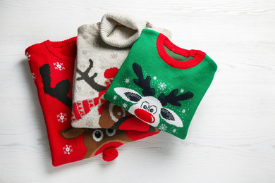 Photo of Folded warm Christmas sweaters on white wooden table, top view