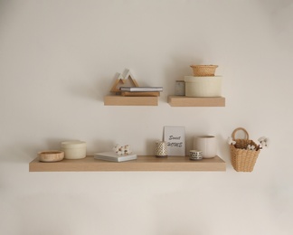 Wooden shelves with books and different decorative elements on light wall