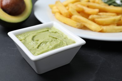 Photo of Plate with french fries, guacamole dip and avocado served on black table, closeup